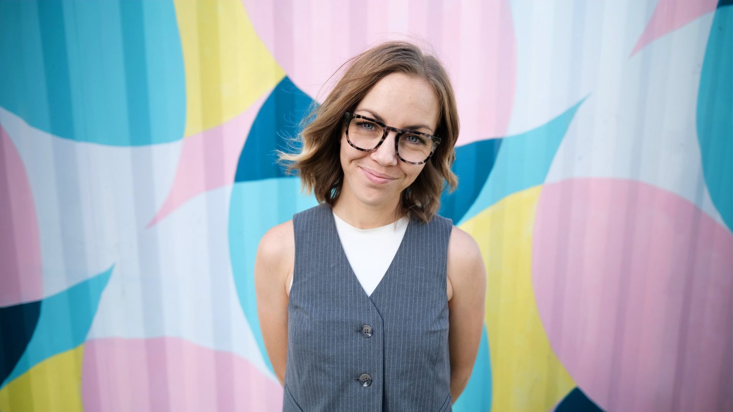 Lauren smiling in front of a colorful pastel mural